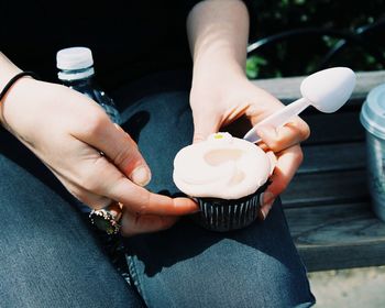 Midsection of woman holding cupcake while sitting on bench