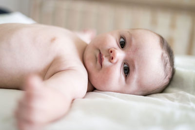 Portrait of cute shirtless baby boy lying on bed at home