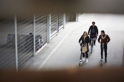 High angle view of male and female teenage friends riding electric push scooters and bicycle on street in city