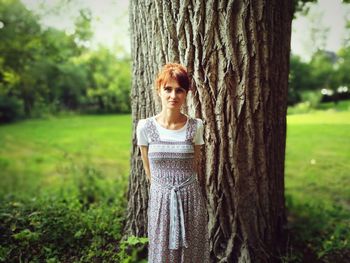 Portrait of young woman standing on tree trunk