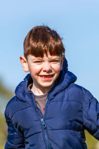 A cute, blue-eyed, redhead boy wearing a blue jacket running on a park on a sunny spring day