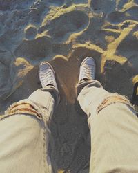 Low section of man standing on sand at beach