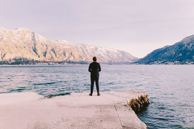 Rear view of man standing at lakeshore against sky