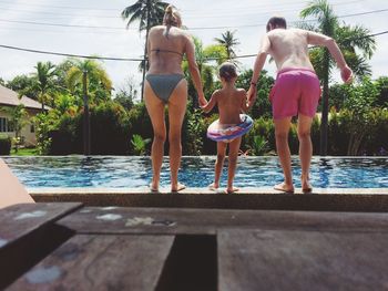 Rear view of parents holding daughter hands while diving in swimming pool during sunny day