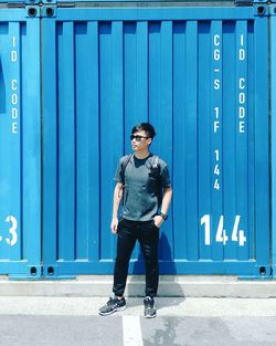 Full length of young man standing against blue wall