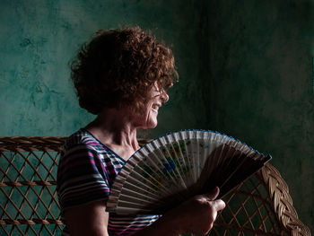 Smiling woman holding hand fan at home