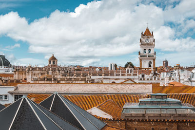 Church amidst buildings against cloudy sky in city