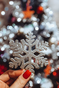 Female hands with french manicure holding a silver christmas toy snowflake on a background