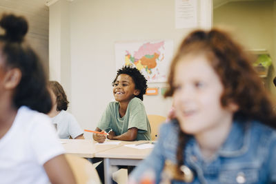 Smiling boy sitting with friends at desk in classroom