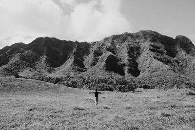 Man with arms outstretched standing on field against mountains
