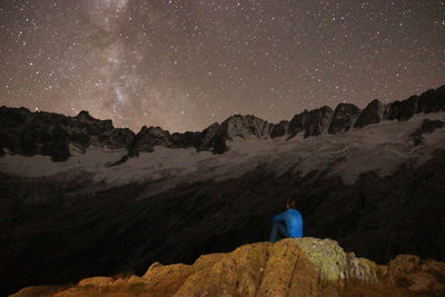 Rear view of man sitting on rock against star field