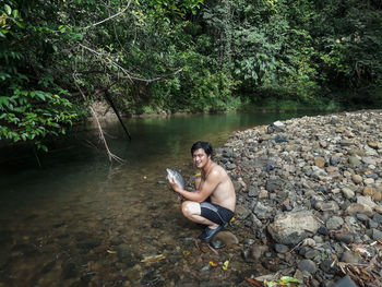 Young woman sitting on rock by lake in forest