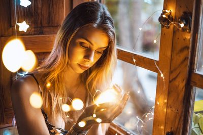 Portrait of young woman looking at illuminated lamp