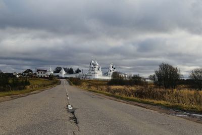 Empty road in city against cloudy sky