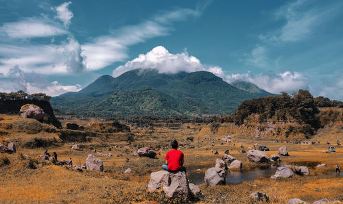 Rear view of people relaxing on mountain against sky