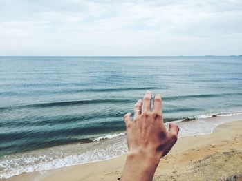 Cropped hand of man gesturing at beach against sky