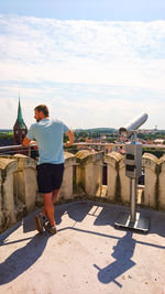 Rear view of young man looking at city against sky during sunny day