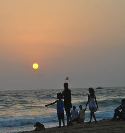 Friends standing on beach against sky during sunset