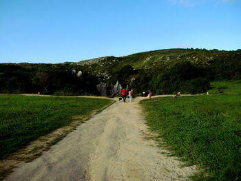 People walking on road against clear blue sky