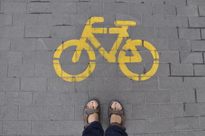 Low section of man standing by bicycle sign on street