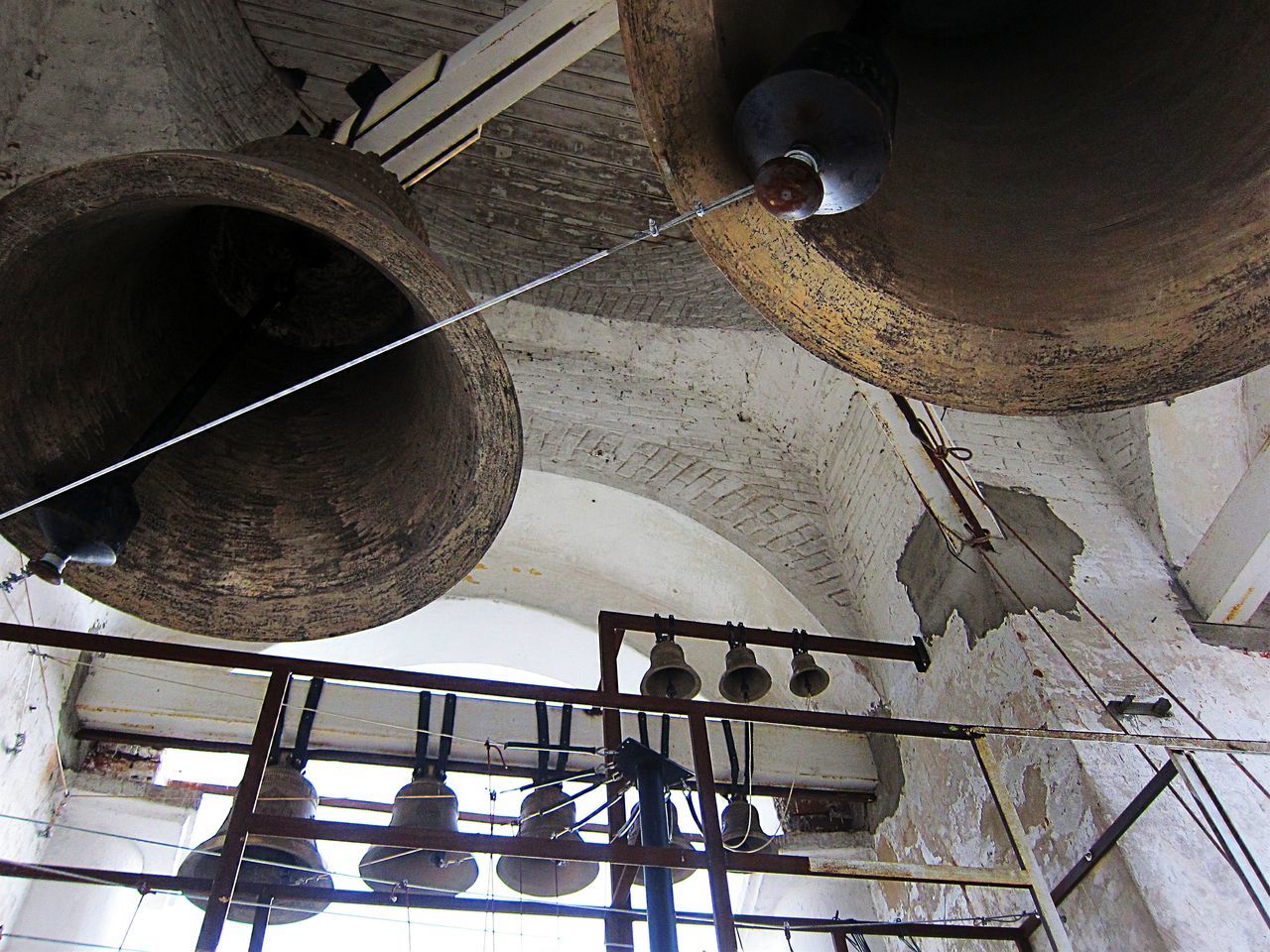 low angle view, architecture, built structure, indoors, lighting equipment, ceiling, metal, building exterior, hanging, old, no people, wall - building feature, circle, electricity, pipe - tube, building, day, electric lamp, railing, metallic