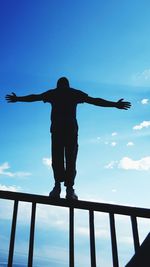 Low angle view of man standing on railing against sky