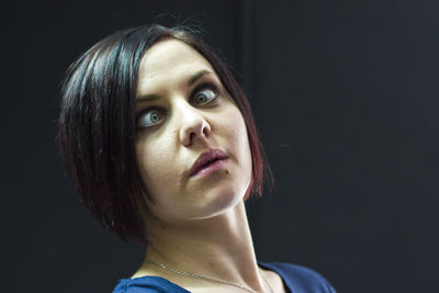 Close-up portrait of cross-eyed young woman against black background