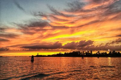 Silhouette people on sea against orange sky