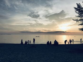 Silhouette people on beach against sky during sunset