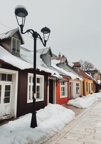 Houses by snow covered street against sky