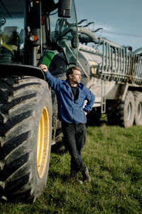 Contemplative mature farmer standing by tractor at farm on sunny day