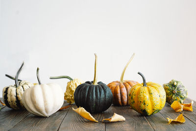 Multicolored pumpkins and dry autumn leaves on wooden background.