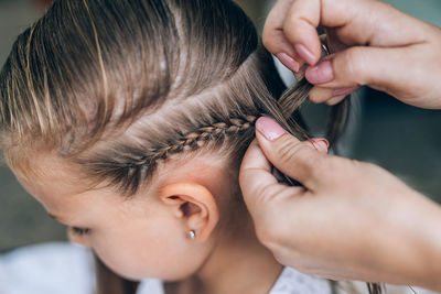 Cropped hands of mother tying daughter hair at home