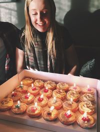 Smiling young woman looking at cupcakes on table at home