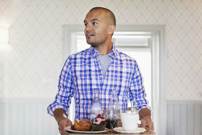 Smiling man holding tray while standing at cafe