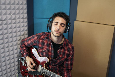 Young man playing guitar against wall