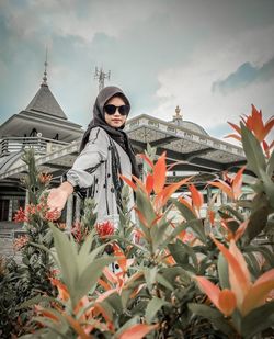 Teenager girl standing by flowering plants against sky