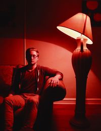 Full length of young man sitting in illuminated room