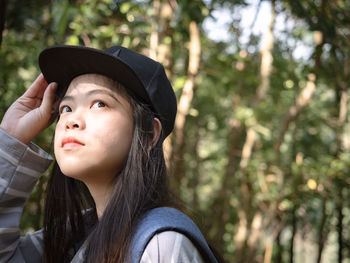 Young woman wearing cap looking away against trees