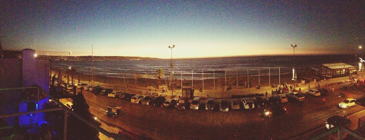 sea, water, beach, horizon over water, sky, sunset, shore, illuminated, incidental people, outdoors, city, large group of people, street light, clear sky, nature, scenics, sand, built structure, lighting equipment, beauty in nature