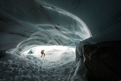 Mountaineer coils climbing rope after rappelling into glacier cave.