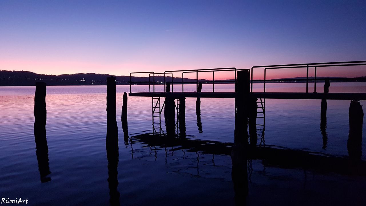 SILHOUETTE WOODEN POSTS IN LAKE AGAINST CLEAR SKY