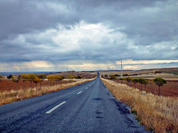 Road amidst field against cloudy sky