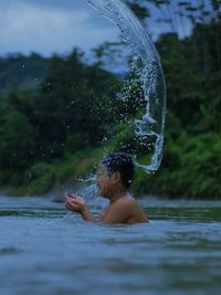 Young shirtless man splashing in river