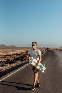 Full length portrait of man standing on road against clear sky