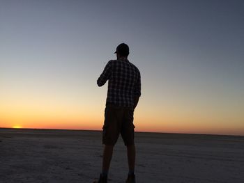 Rear view of man standing at beach against clear sky