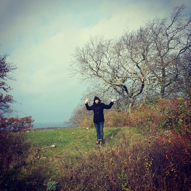 full length, lifestyles, tree, rear view, sky, leisure activity, grass, standing, casual clothing, tranquility, walking, tranquil scene, field, nature, bare tree, cloud - sky, growth, person