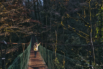 Rear view of woman on footbridge in forest