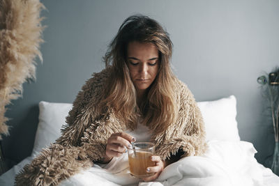 Close-up of woman holding lemon tea sitting on bed