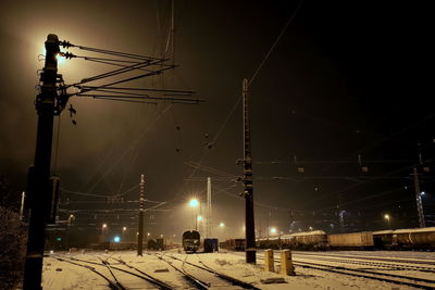 Illuminated railroad tracks against sky during winter at night